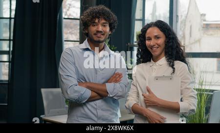 Two smiling entrepreneurs colleagues multiracial team Arabian man businessman Indian woman businesswoman business partners crossed hands pose look at Stock Photo
