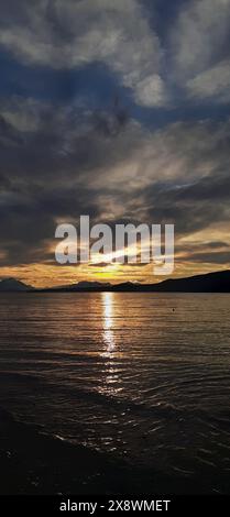 Dramatic sunset over a calm sea with dark clouds partially obscuring the sun and the light reflecting on the water Stock Photo