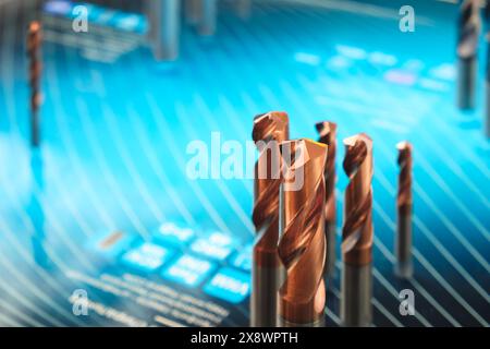 A close up of a blue background with a group of metal drill bits on it. The drill bits are all different sizes and shapes, with some being larger and Stock Photo
