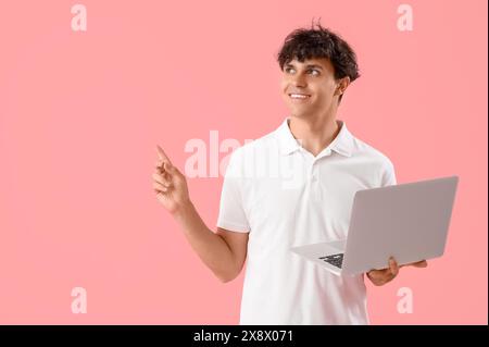 Male programmer with laptop pointing at something on pink background Stock Photo
