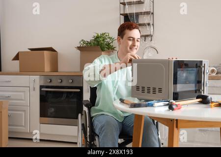 Young man in wheelchair repairing microwave oven at home Stock Photo