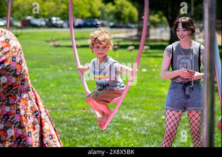 A child wearing a t-shirt with the words 'Everyone' in the colors of the Progress Pride flag enjoys a heart shaped swing at Placer Pride in Royer Park Stock Photo