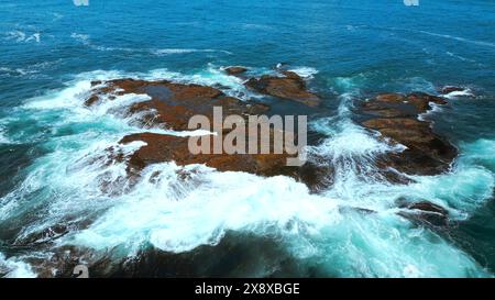 Aerial view of ocean waves crashing into rocks. Clip. Flying above turquoise water and giant boulders. Stock Photo