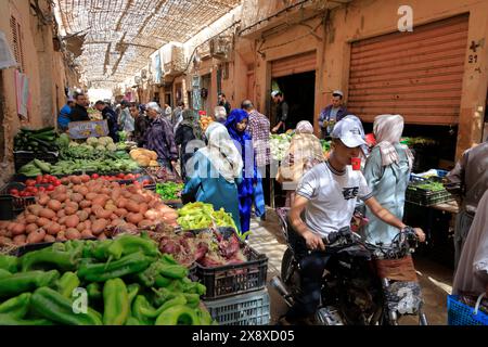 Vegetable sellers in Ghardaia market with a shopper on his motorcycle and hold his coffee cup in his mouth in foreground. Mazb Valley.Ghardaia Province.North Sahara.Algeria Stock Photo