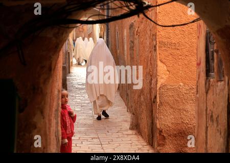 Mozabite women in white haik walking in a narrow street inside of Ksar El Atteuf with a young girl in foreground.Mzab Valley.Ghardaia Province.North Sahara.Algeria Stock Photo