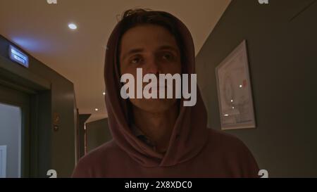 Young man in pink oversize hoodie at the hotel. Stock clip. Man walking along room doors in long corridor. Stock Photo