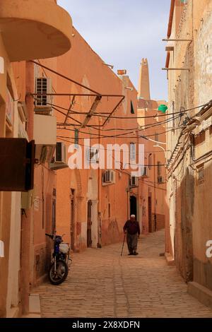 An old man walking the street of Beni Isguen with traditional architectures and the minaret of grand mosque in the background.Beni Isguen is one of the 5 Ksars (fortified settlement) in Mzab valley.Ghardaia province.North Sahara.Algeria Stock Photo