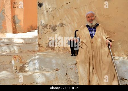 An old Mozabite man in traditional clothing with two cats in Ksar Beni Isguen.Beni Isguen is one of the 5 Ksars (fortified settlement) in Mzab valley.Ghardais Province.North Sahara.Algeria Stock Photo