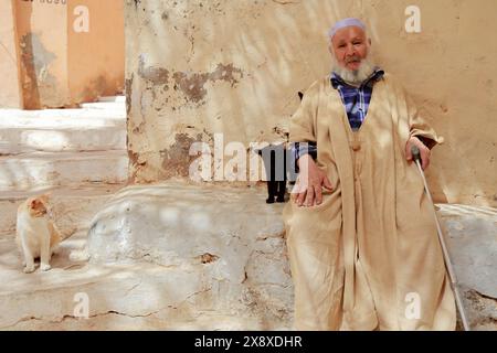 An old Mozabite man in traditional clothing with two cats in Ksar Beni Isguen.Beni Isguen is one of the 5 Ksars (fortified settlement) in Mzab valley.Ghardais Province.North Sahara.Algeria Stock Photo