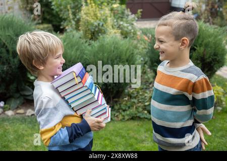 Two boys, classmates, friends are standing opposite each other, one child is holding a large stack of books in his hands. cute schoolchildren 8 years Stock Photo