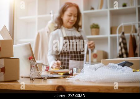 A selective focus image of a shopping cart model, cardboard boxes, bubble wrap, computer, and equipment on a table with a blurred background of a matu Stock Photo