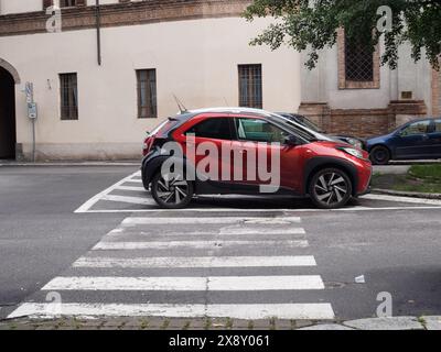 Cremona, Italy - May 15th 2024 Red compact Toyota Aigo crossover suv parked next to a zebra crossing on an urban street, with buildings and cars in th Stock Photo