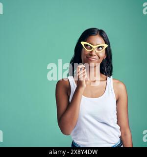 Girl, gen z and thinking with glasses in studio on green background for fashion, trendy and style for fun. Female person, expression and pose for Stock Photo