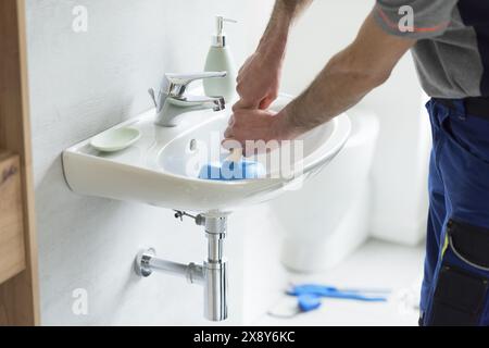 Repairman unclogging a bathroom sink using a plunger Stock Photo