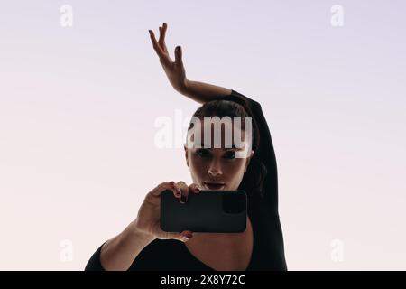 Confident female performer recording a selfie video of her dance routine with a smartphone. With expressive dance moves, she captures her unique style Stock Photo
