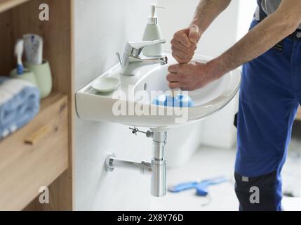 Repairman unclogging a bathroom sink using a plunger Stock Photo