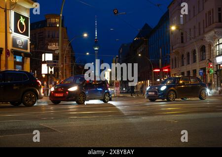 Cars driving down night Oranienburger street, Illuminated buildings and Fernsehturm TV tower visible in background, Nightlife, sustainability and envi Stock Photo