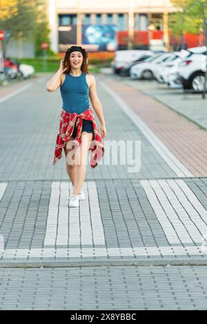Energetic young woman with curly hair walks cheerfully in an urban area, flannel tied around waist.  Stock Photo