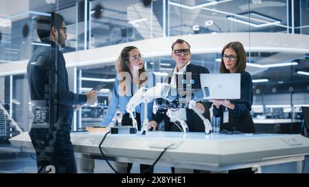 Robotics Engineer, Project Manager and Machinery Operators Collaborate on a Robot Canine Project, Standing with Laptop Computer in Scientific Technology Lab. Young Team Developing an AI Robotic Dog. Stock Photo