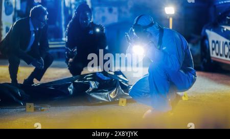 Man from Forensics Team Taking Photos of Evidence and Victim's Body in a Crime Scene at Night. Professional Investigators and Police Officers Working to Solve the Case of Potential Premeditated Murder Stock Photo