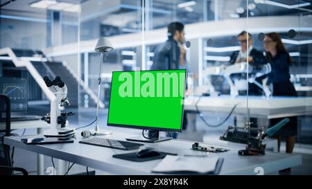 Industrial Research Laboratory with Desktop Computer with Green Screen Mock Up Display. Scientific Lab, Engineering Research Center with Specialists Working on Robot Development in the Background. Stock Photo