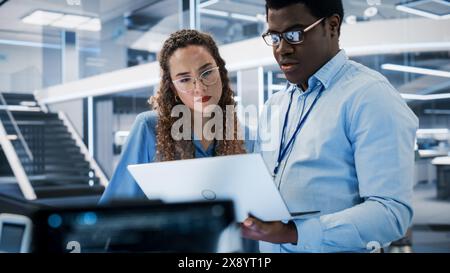 Portrait of Two Young Diverse Engineers Use Computer to Connect, Analyze and Discuss How to Program a Robot Dog. High Tech Research Laboratory with Modern Equipment. Stock Photo
