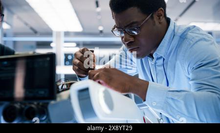 Close Up Portrait of an African American Robotics Engineer Setting Up a Robot Dog Prototype, Using a Screwdriver to Fasten the Bolts. Scientist Connect a Motherboard to a Mobile AI Four-Legged Robot. Stock Photo