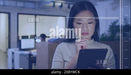 Image of interface with data processing against asian woman using digital tablet at office Stock Photo