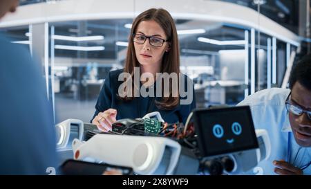 Two Industrial Robotics Engineers Gathered at a Table With Robotic Mobile Prototype. Two Females Discuss the Project, Program the Robot Dog with a Laptop Computer. Stock Photo