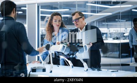Robotics Engineer, Project Manager and Machinery Operators Collaborate on a Robot Machine Project, Standing with Laptop Computer in Scientific Technology Lab. Young Team Developing an AI Robotic Dog. Stock Photo