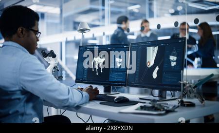Black Robotics Engineer Working on Programming a Robot Dog on Desktop Computer. Young Team of International Industrial Science Specialists Developing a Mobile Robot in the Background. Stock Photo
