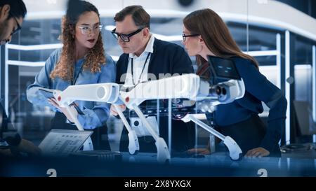 Robotics Engineer, Project Manager and Machinery Operators Collaborate on a Robot Canine Project, Standing with Laptop Computer in Scientific Technology Lab. Young Team Developing an AI Robotic Dog. Stock Photo