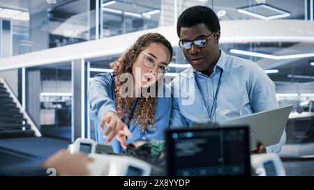 Portrait of Two Multicultural Industrial Robotics Engineers Using Laptop Computer to Work on a Robot Dog. Colleagues Setting Up the Interface for a Mobile AI Robot Concept. Stock Photo