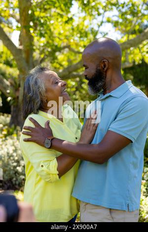 A diverse senior couple embracing outdoors, wearing casual shirts Stock Photo