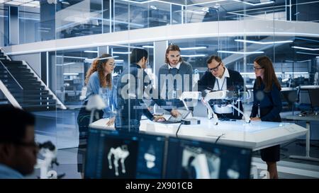 Robotics Engineer, Project Manager and Machinery Operators Collaborate on a Robot Canine Project, Standing with Laptop Computer in Scientific Technology Lab. Young Team Developing an AI Robotic Dog. Stock Photo