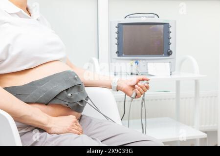 A pregnant woman performing cardiotocography (CTG) to monitor fetal heartbeat and uterine contractions during the final weeks of pregnancy Stock Photo