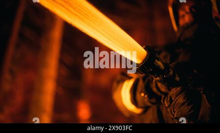 Close Up Low Angle Creative Portrait of a Brave African American Firefighter Using a Firehose to Fight a Forest Fire. Focus on Black Fireman Hands Holding High-Pressure Water Hose. Stock Photo