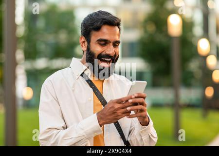 Joyful Man in City Park Using Smartphone on Sunny Afternoon Stock Photo