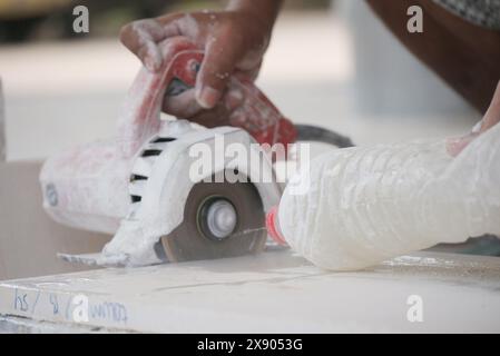 A detailed close-up captures a skilled craftsman using a handheld power saw to precisely cut a tile, with dust and debris scattered around. The focus Stock Photo