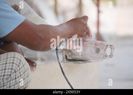 A detailed close-up captures a skilled craftsman using a handheld power saw to precisely cut a tile, with dust and debris scattered around. The focus Stock Photo