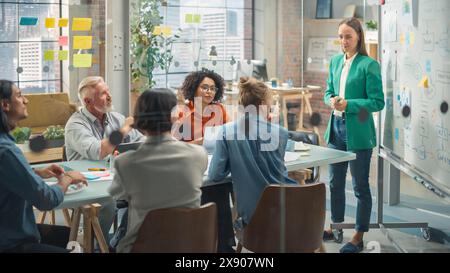 Collaborative Multiethnic Team Group Attending a Meeting to Develop a Strategy. Young Female Manager Using a Whiteboard to Explain Plan Steps. Colleagues Following her Presentation Stock Photo
