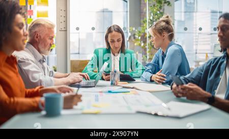 Office Meeting in Conference Room: Diverse Team of Professional Businesspeople Talking about Firm Strategy. Ambitious, Creative Start-up Team Using Laptop and Smartphones, Designing, Planning Stock Photo