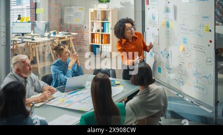 Diverse Modern Office: Black Businesswoman Leads Business Meeting with Managers, Talks, Explains Statistics, Uses a Whiteboard with Graphs, Big Data. Digital Entrepreneurs Work on eCommerce Project Stock Photo