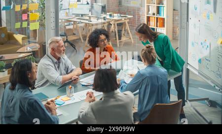 Female Chief Analyst Holds Meeting Presentation for a Team of Economists. She Shows a Whiteboard with Growth Analysis, Charts, Statistics and Data, Answers Questions. People Work in Creative Office Stock Photo