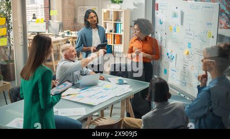 Diverse Modern Office: Black Businesswoman Leads Business Meeting with Managers, Talks, Explains Statistics, Uses a Whiteboard with Graphs, Big Data. Digital Entrepreneurs Work on eCommerce Project Stock Photo