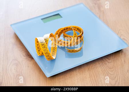 Closeup of a home scale and measuring tape on top of the blue scale on a wooden floor. Stock Photo