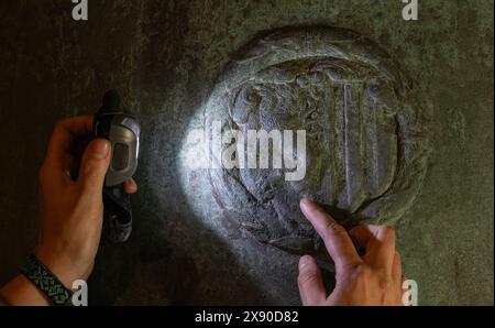 28 May 2024, Saxony, Leipzig: In the belfry of St. Thomas Church in Leipzig, Christina Neubacher, a qualified restorer, examines an exposed coat of arms of the city of Leipzig on the Hilliger bell from 1574. Since the end of April, renewed work has been taking place in the bell chambers to restore and conserve the surfaces of the historic bells. In addition, the bells have now been measured using a special 3D scanning process in order to digitize the cross-sections and details of the decorations. The surface restoration and digitization project will preserve and document one of the most import Stock Photo