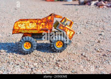 Close-up of a small, yellow, rusted toy dump truck isolated on a gravel surface. Stock Photo