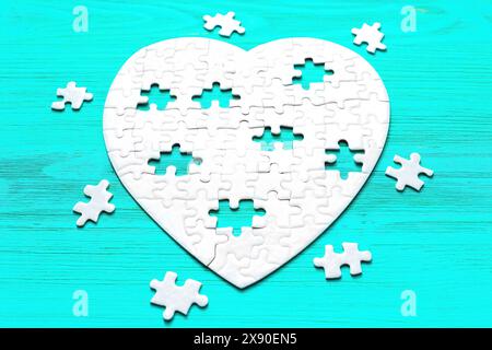 Incomplete heart-shaped puzzle set against a serene blue wooden backdrop. The missing puzzle pieces are scattered around the heart. Love and connectio Stock Photo