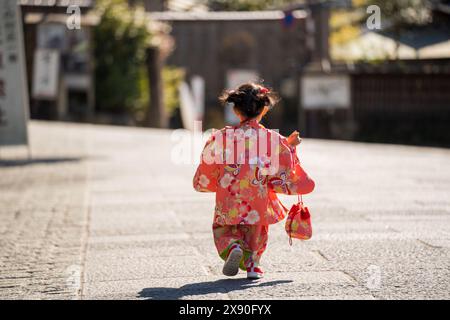 A little girl in a kimono is running down a street. Stock Photo